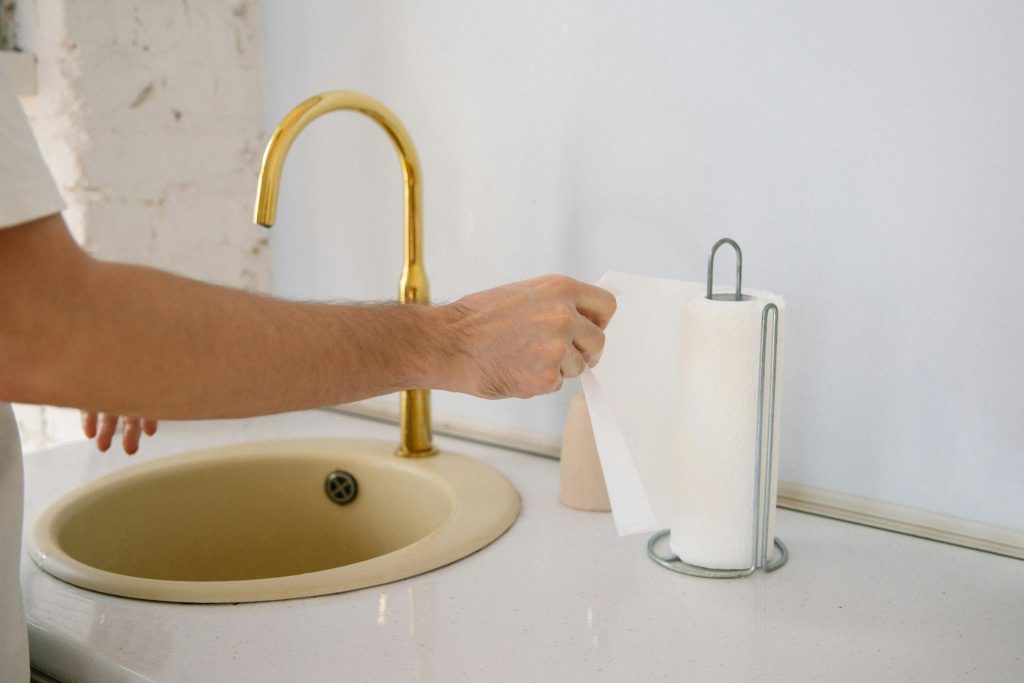 A man pulling a paper towel from a dispenser near the sink